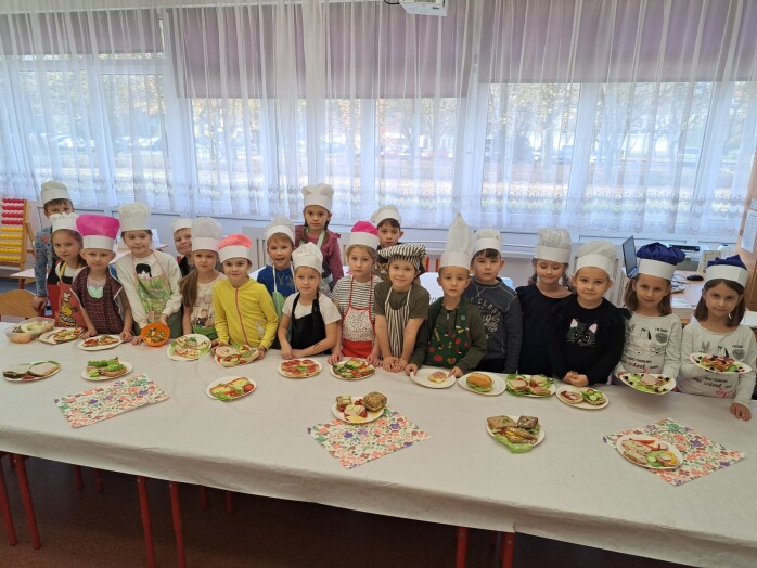 Uczniowie klasy1d stoją przy stole, na którym znajdują się talerzyki z kanapkami przygotowanymi przez dzieci.