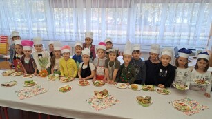 Uczniowie klasy1d stoją przy stole, na którym znajdują się talerzyki z kanapkami przygotowanymi przez dzieci.