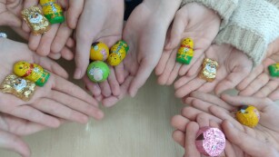 Zdjęcie 1 przedstawia dłonie dzieci na których leżą jajka czekoladowe w zielono-żółtym opakowaniu